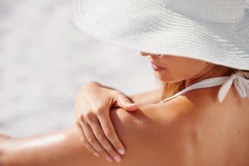 belle femme à la peau saine application de crème solaire à l'épaule