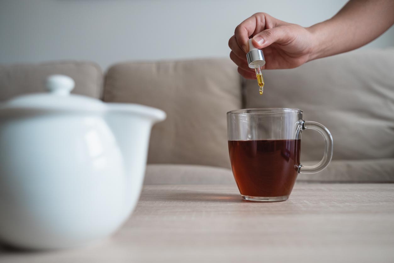 Femme ajoutant la goutte de cbd dans la tasse de thé avec la pipette