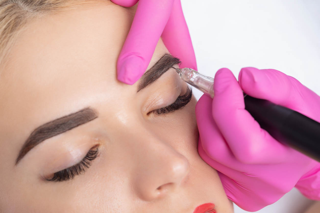 Maquillage permanent pour sourcils de belle femme blonde dans le salon de beauté. Esthéticienne de plan rapproché faisant le tatouage de sourcils