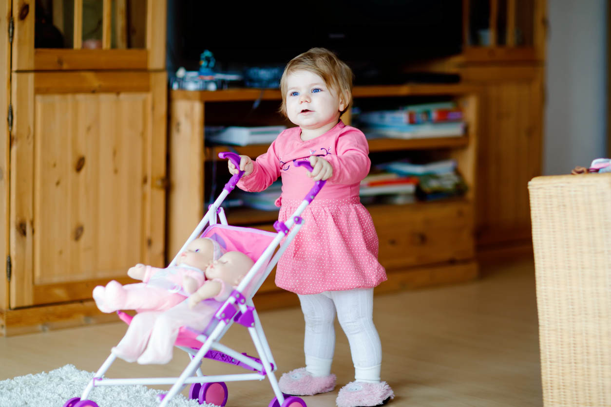 Belle poussette d’enfant en bas âge poussant avec un jouet à la maison. Enfant heureux avec deux poupées