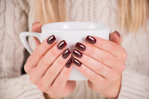 Femme avec vernis à ongles brun tient la tasse de café