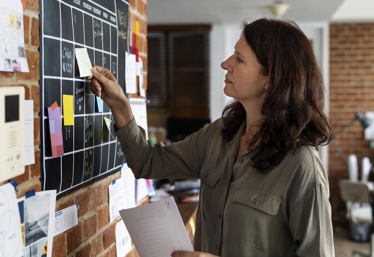 Femme qui colle un post-it sur un tableau noir