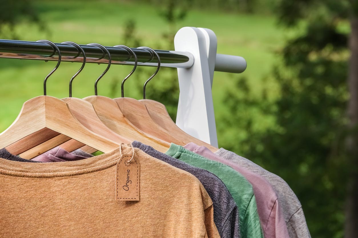 êtements biologiques, t-shirts, suspendus sur des cintres en bois avec le vert de la forêt