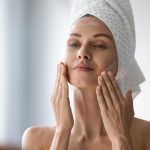 femme sortat de la douche se met de la crème sur le visage dans le miroir