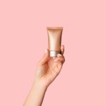 Main de femme affichant la bouteille d' autobronzant sur le fond rose