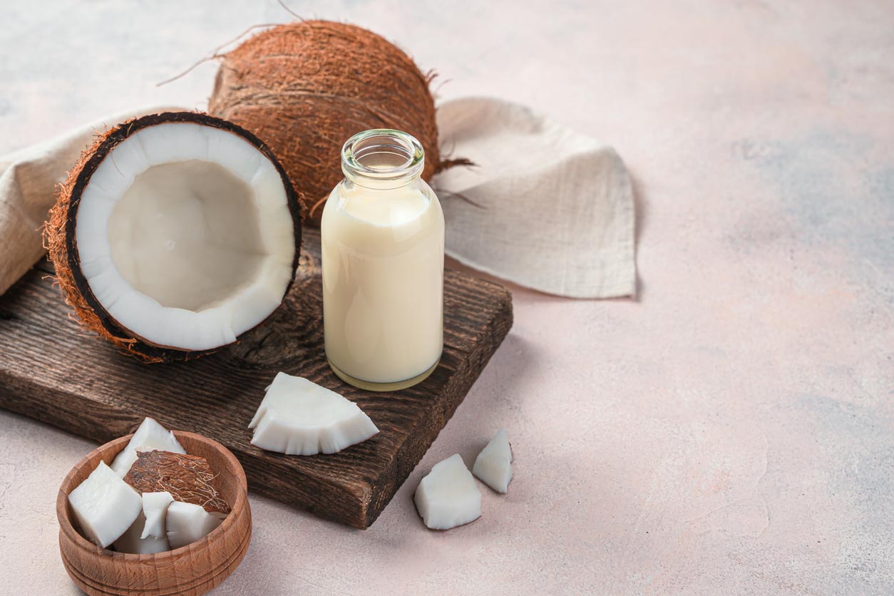 Bouteille de lait de coco sur une planche avec noix de coco cassées à côté