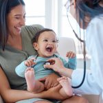 Photo d’un bébé assis sur les genoux de sa mère alors qu’il est examiné par un médecin