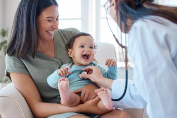 Photo d’un bébé assis sur les genoux de sa mère alors qu’il est examiné par un médecin