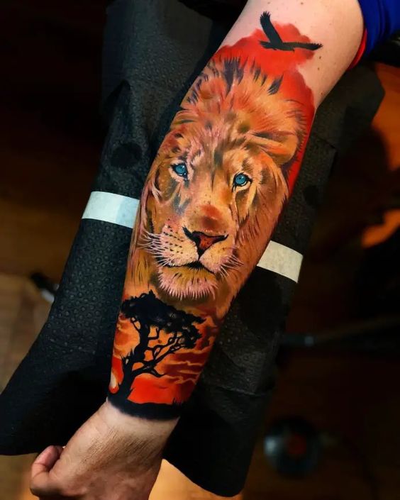 Tatouage Tête De Lion Avec Corbeau Et Savane Sur L’avant Bras