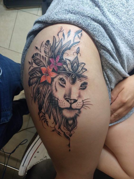 Tatouage Lionne Avec Couronne, Plumes Et Fleurs Sur La Cuisse