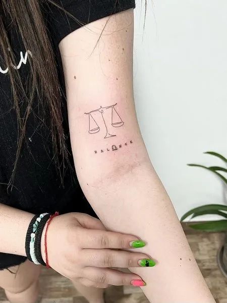 Tatouage Balance En Trait Unique Avec Mot Sur Le Bras